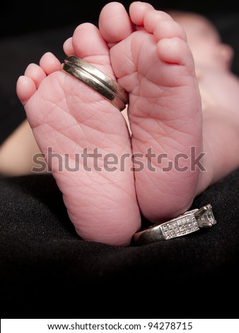  Close up of a newborn girls feet with her parent's wedding ring's on