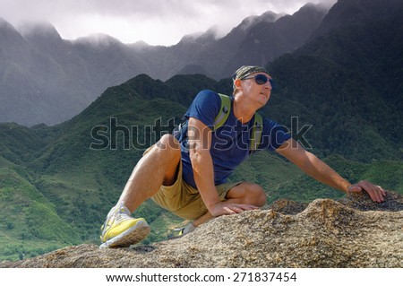 Young man climbs the mountain on the background of the valley in the clouds
