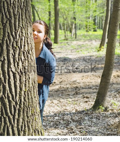 Young cute girl peeking from behind a tree during a walk in the park