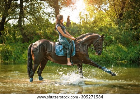 Woman on horseback rides along the river on a hot summer day.