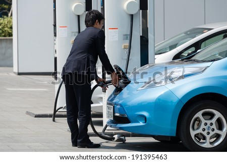 YOKOHAMA, JAPAN - APRIL 24, 2014: A businessman plugs in an electric car Nissan Leaf to charge the car at a charging station in front of the entrance of Nissan\'s Global Headquarters.