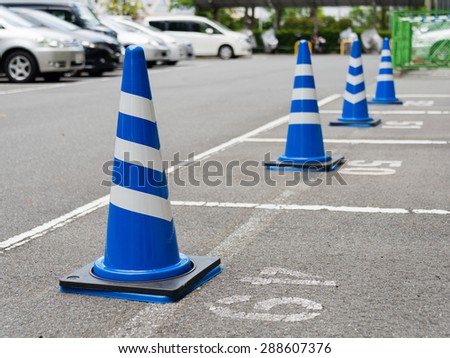 Traffic cones painted in blue and white standing at parking lot. There are cars parked in the distance.