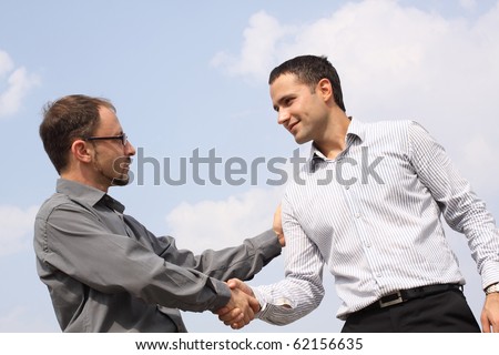 Closeup of two young businessmen shaking hands over a deal on sky background
