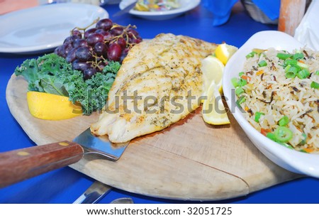 Grilled white fish served with rice, lemons and grapes on the wood cutter plate.