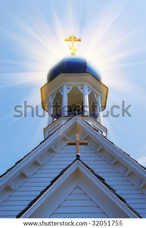 Sun rays shining up from gold cross on a small  old Christian orthodox Church.
