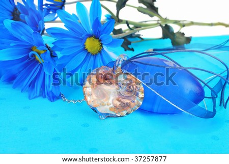 Beautiful hand cut and fired  heart  glass pendant  with fantastic blue flowers are on the bright blue napkin background.  (It's nice present idea).