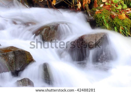 Cascading Waterfall and autumn leaves closeup very smooth water with wet rocks.  Fall river landscape.