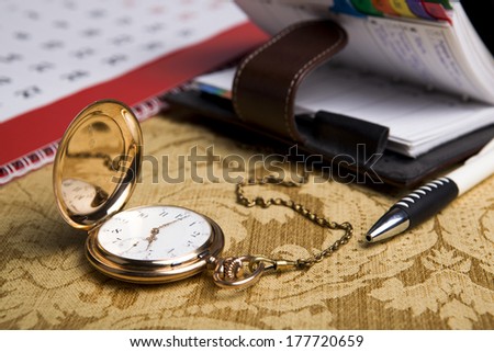 Gold pocket watch with wall calendar and sketchpad, pen close-up