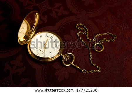 Gold pocket watch on on maroon cloth close-up