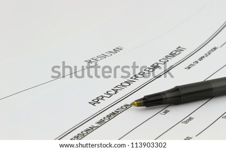 Blank employment application with resume and pen on desk.