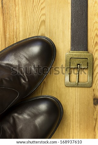 Stylish brown leather shoes and belt accessories on wood background.