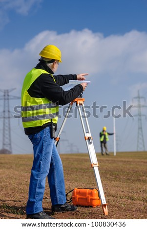 Land surveyors measuring with tacheometer point direction looking at plan