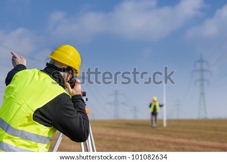 Land surveyors measuring with tacheometer speaking through transmitter construction site