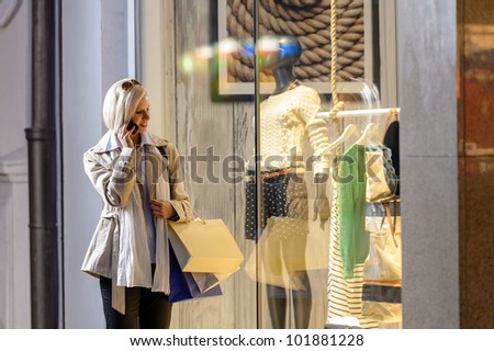 Young woman shopping evening city looking into shop windows phone