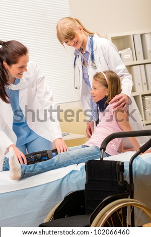 Two female doctors examine broken leg little girl wheelchair