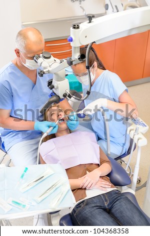 Dentist operating female patient through microscope at surgery office