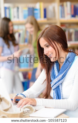 Female brunette student at high school library working on laptop