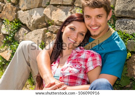 Young couple in love sitting leaning against wall sunny day