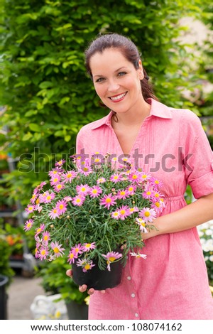 Smiling woman holding pink potted flower in garden center greenhouse