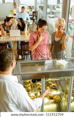 Waiter showing women cakes on window display cafe smiling friends