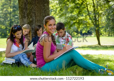 Students studying on meadow in park teens writing reading campus