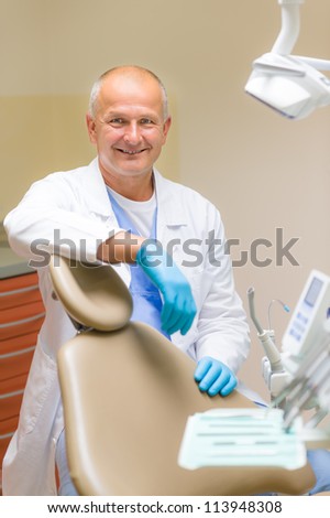 Portrait of mature smiling dentist sitting in modern dental surgery