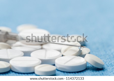 Hypodermic needle with drip medication spilled capsules on blue background