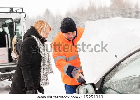Woman mechanic looking under car hood snow assistance winter broken