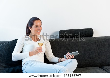 Happy woman lying down couch watching TV drinking wine