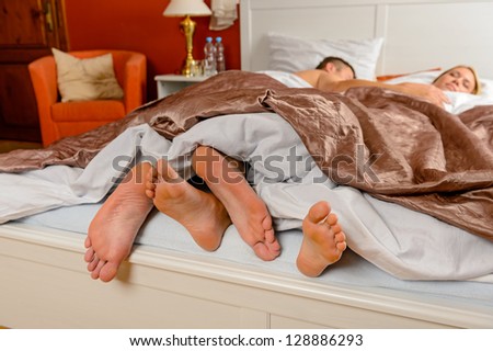 Lovers foot poking out bed covers sleeping couple