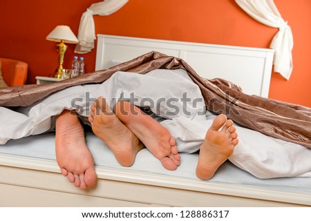 Napping man woman barefoot lying under covers bed hotel room