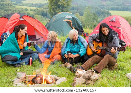 Girls on vacation camping with tents listening girl playing guitar