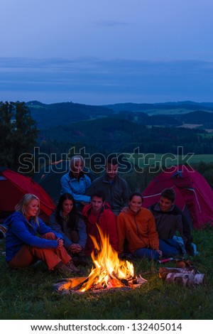 Friends watching fire together beside camp and tents in dark