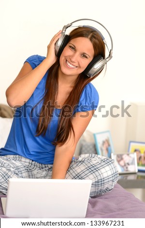 Cheerful teenager girl listening music with headphones on laptop