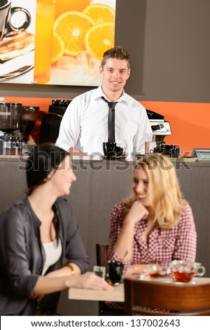 Attractive bartender smiling in pub female customers talking
