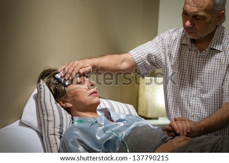 Caring senior man helping his sick wife lying in bed