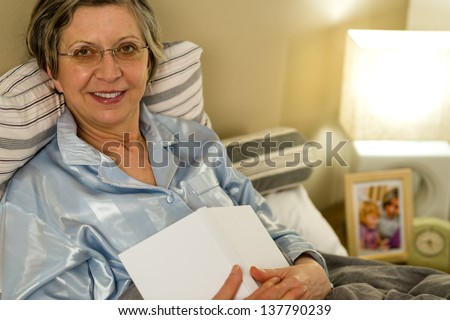 Old woman in pajamas lying in bed looking at camera