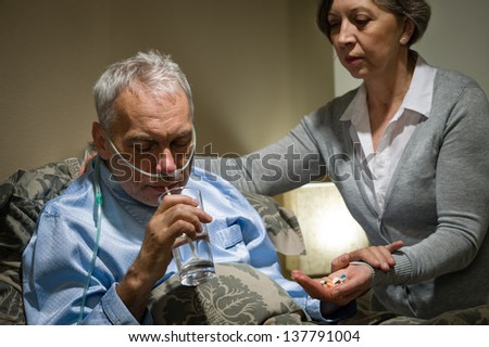 Senior man taking medication with water caring wife helping