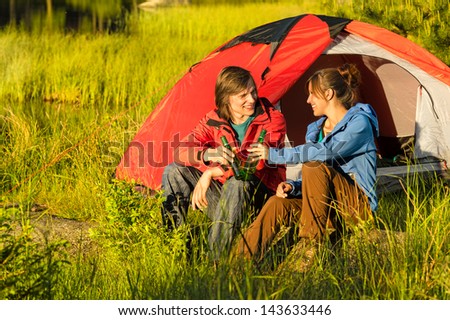 Camping teenagers drink beer outdoors sunset on the meadow