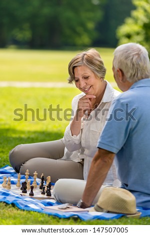 Elderly friends couple playing chess in park on sunny day