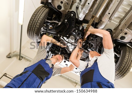 Auto mechanics working underneath a lifted car
