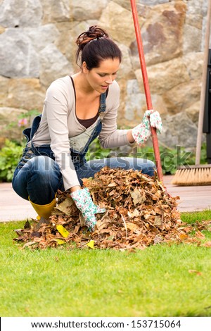 Young woman raking dry leaves pile backyard housework fall