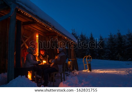 Evening winter cottage friends enjoy hot drinks in snow countryside