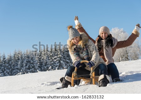 Two Girlfriends Sledge Downhill In Sunny Wintertime Snow Wooden Sledge