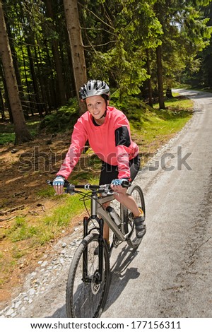 Woman mountain biking in sunny forest cycling path smiling