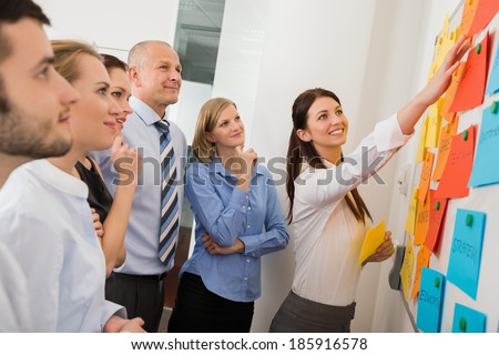 Businesswoman pointing on whiteboard in meeting with office colleagues