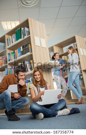 University classmates studying together on laptop with friends in library
