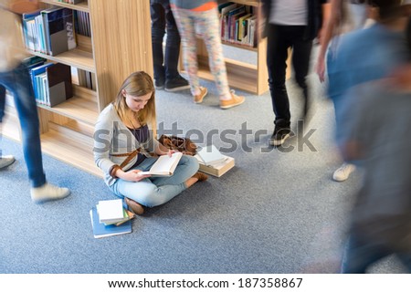 Student sitting on floor in library classmates walking blur motion