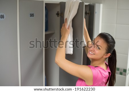 Smiling young woman placing towel on locker door at gym