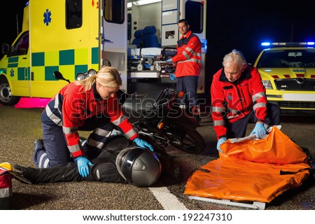 Emergency team assisting injured motorbike man driver at night